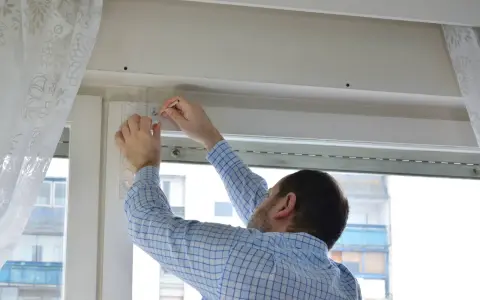Hombre con camisa a cuadros midiendo para reparar persianas.