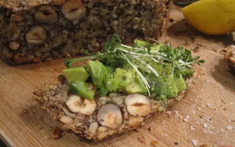 Ein Stück herzhaftes Flohsamenschalen Brot mit Nüssen, belegt mit Avocado und Kresse. Ein gesunder Genuss!