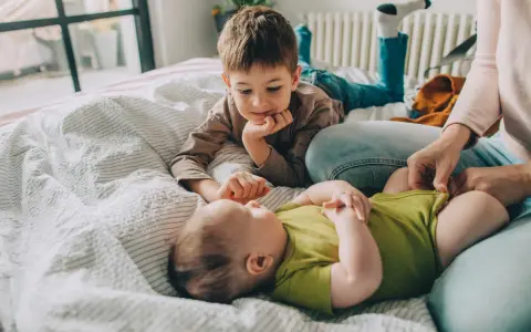 Starszy brat patrzy z czułością na niemowlę. Zastanawiamy się, ile cm rośnie dziecko w ciągu roku, obserwując te małe nóżki.