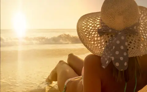 Donna con cappello di paglia e un bikini a pois, godendosi il tramonto sulla spiaggia. La sua pelle ha una perfetta abbronzatura arancione.