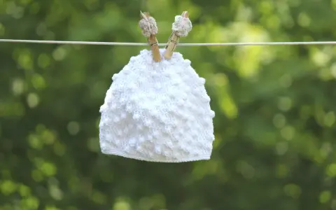Vit virkad mössa med popcornmaskor hänger på en lina.