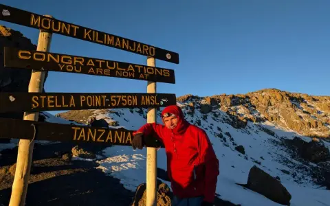 Mężczyzna w czerwonej kurtce przy znaku "Mount Kilimanjaro, Stella Point". To właśnie tutaj jest Kilimandżaro!