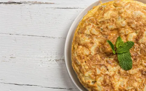 Frittata di cipolle dorata e soffice, guarnita con foglie di menta fresca, su un piatto bianco appoggiato su un tavolo di legno sbiancato.