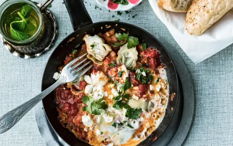 Herzhaftes Menemen ohne Ei mit Artischocken und Feta, garniert mit Petersilie. Dazu frisches Brot und Minztee.
