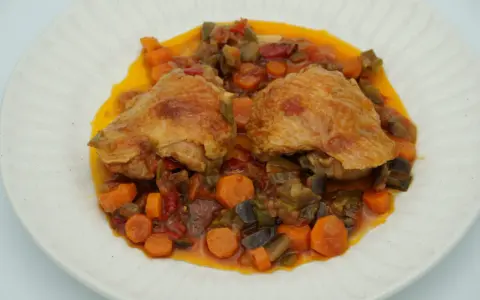Dos piezas de pollo dorado sobre un guiso de verduras coloridas, zanahorias y berenjenas. Un delicioso pollo a la jardinera.