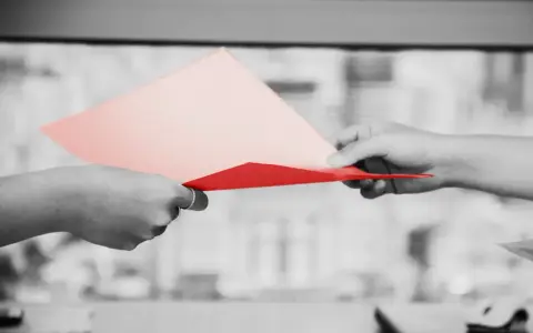 Dwie dłonie przekazują sobie dokumenty. Jedna z nich trzyma różową kartkę, druga czerwoną. Symbolizuje to uprawomocnienie postanowienia sądu.