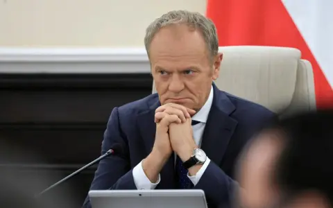 Mężczyzna w garniturze, z zaciętą miną, wygląda jak pesymista. Dłonie splecione, wzrok utkwiony w dal.