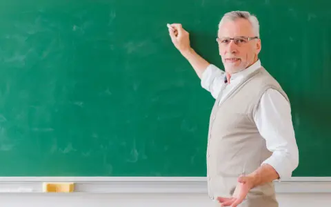 Doświadczony nauczyciel akademicki z kredą w dłoni, tłumaczy coś przy zielonej tablicy.