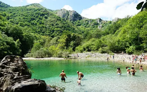 Gente disfrutando del agua cristalina en la olla de San Vicente, rodeada de exuberante vegetación y montañas.