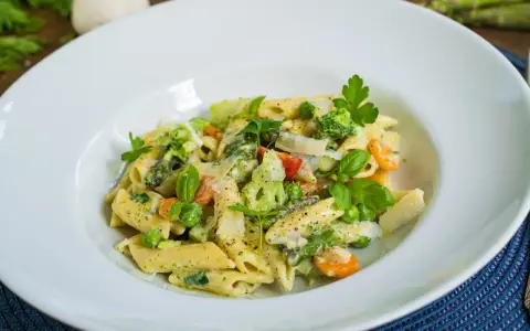 Penne mit cremigem Pesto, Spargel, Erbsen, Brokkoli und Karotten, garniert mit Parmesan und frischen Kräutern.