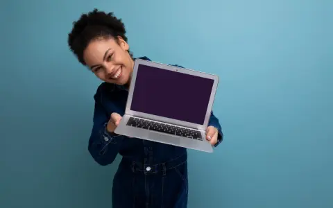 Uśmiechnięta kobieta prezentuje laptopa, gotowa do sprzedaży. Dowiedz się, jak przygotować laptop do sprzedaży, by uzyskać najlepszą cenę.