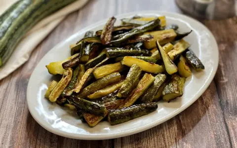 Zucchine al forno dorate e saporite, tagliate a bastoncini e servite su un piatto bianco.