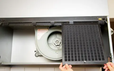 Mains d'une personne retirant un filtre à charbon d'une hotte aspirante pour le nettoyer.