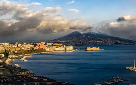 Vista panoramica di Napoli con il Vesuvio innevato sullo sfondo, il Castel dell'Ovo e il lungomare.