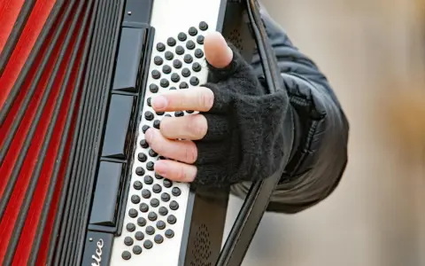 Dłoń w rękawiczce gra na akordeonie, wydobywając dźwięki tego wyjątkowego instrumentu.