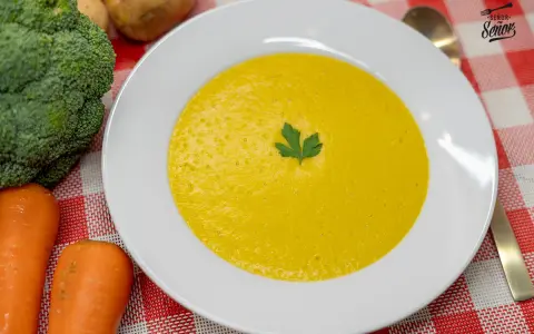 Un cremoso puré de verduras, con brócoli y zanahorias frescos al lado, listo para disfrutar.