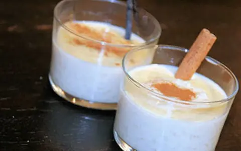 Deux verres de riz au lait crémeux, saupoudrés de cannelle. Un bâton de cannelle décore l'un des desserts, parfait pour une recette de riz au lait.