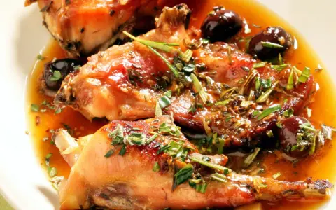 Coniglio alla ligure succulento, con olive nere e erbe aromatiche, servito in un piatto bianco.