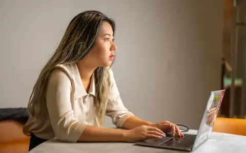 Młoda kobieta, analityk, skupiona na pracy przy laptopie. Jej wzrok skierowany jest w dal, jakby analizowała złożone dane.
