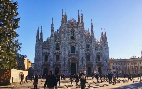 Le majestueux Duomo di Milano se dresse sous un ciel bleu, entouré de passants et d'un sapin de Noël décoré.