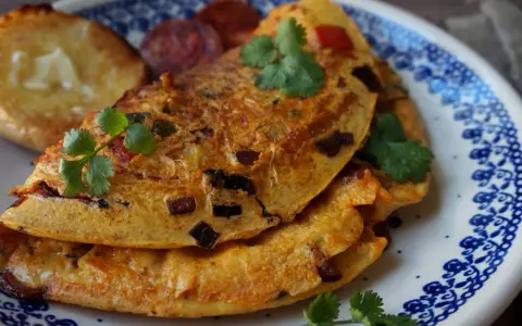 Pyszny omlet z chorizo, podany z grzankami i świeżą kolendrą, na talerzu z niebieskim wzorem.