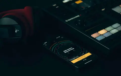 Czerwone słuchawki, kontroler Maschine i smartfon z aplikacją do tworzenia muzyki, gdzie widać koala sampler.