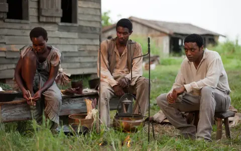 Tre persone sedute all'aperto, in un'ambientazione che ricorda i film biografici sulla schiavitù.