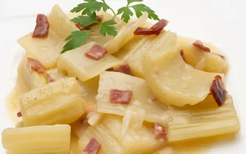 Cardo a la navarra, un plato tradicional con trozos tiernos de cardo en una cremosa salsa, adornado con trocitos de jamón y perejil fresco.