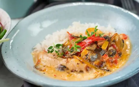 En krämig kyckling- och risrätt med paprika och svamp, garnerad med färska örter. En härlig måltid som ser utsökt ut.