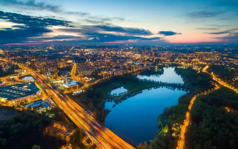 Widok z lotu ptaka na rozświetlone miasto nocą, z autostradą i trzema stawami w tle.