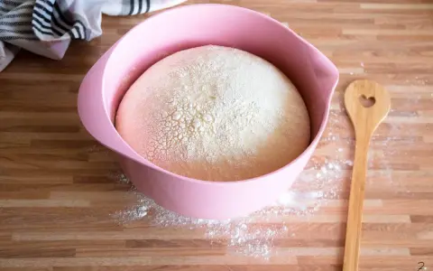 Ein aufgegangener Hefeteig in einer rosa Schüssel, bereit für neue Backideen. Daneben liegt ein Holzlöffel mit Herz.