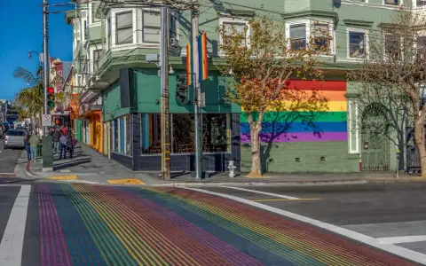 A vibrant rainbow crosswalk leads to a building adorned with a large rainbow mural, a symbol of the gay bed breakfast scene in San Francisco.