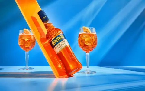 Aperol, znany z orzeźwiającego smaku, ma 11% alkoholu. Na zdjęciu butelka i dwa drinki z pomarańczą.