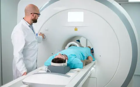 Lekarz nadzoruje badanie rezonansem kolana pacjenta leżącego w aparacie MRI.