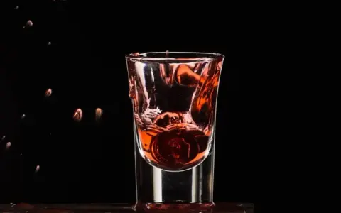 Wściekły pies drink, moneta spada do kieliszka z czerwonym płynem, tworząc fontannę.