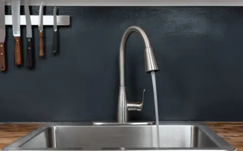 Moderner Küchenwasserhahn für Untertischboiler, der Wasser in ein Spülbecken laufen lässt. Messer hängen an der Wand.
