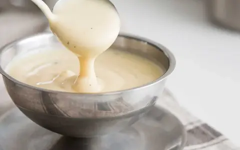 Krämig vaniljsås hälls upp ur en slev i en skål. Perfekt till efterrätt, här är ett enkelt vaniljsås recept.