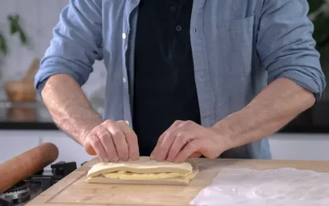 Un homme plie une pâte feuilletée professionnelle sur une planche en bois, prêt à créer des couches parfaites.