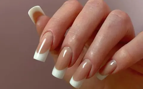 Dłoń z paznokciami w stylu odwrócony french. Klasyczny manicure z białym wykończeniem i naturalnym kolorem płytki.