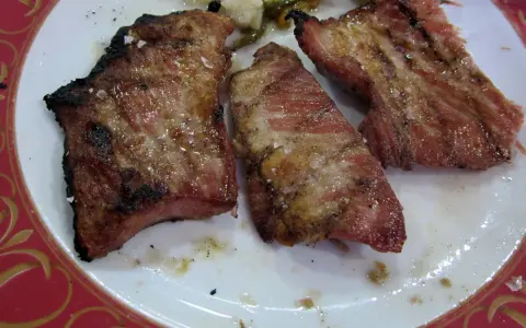 Tres trozos de lomo de cerdo al horno jugoso, con costra dorada y sal gruesa, servidos en un plato blanco con borde rojo.