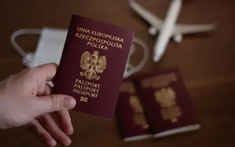 Dłoń trzyma polski paszport. Obok leżą kolejne paszporty, maseczka i samolot. Zastanawiasz się, ile się czeka na paszport?