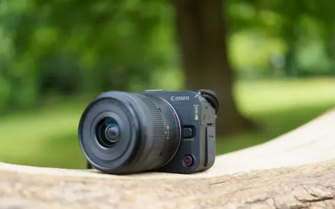Un appareil photo Canon EOS R50, prêt pour un test en extérieur. Le soleil brille sur son objectif.