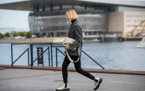 Kobieta w czarnych spodniach i marynarce idzie, a jej biała cholewka buta z grubą podeszwą przyciąga wzrok.