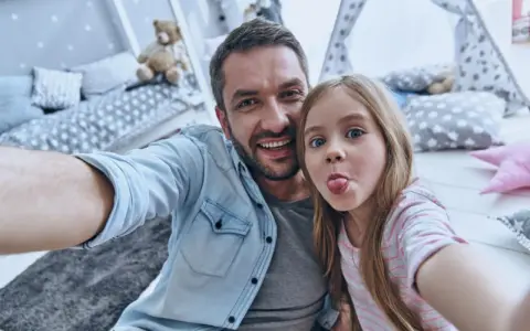 Padre e figlia si scattano un selfie giocoso, un'immagine che cattura la gioia del loro rapporto padre-figlia, quasi come in un'interpretazione freudiana della felicità.
