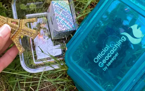 Złoty model Wieży Eiffla w pojemniku, obok niebieskiego pojemnika z napisem "Official Geocaching". To jest geocaching co to za zabawa!