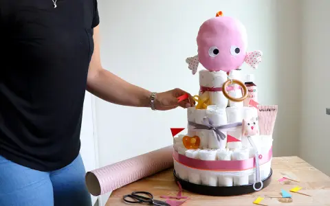 En person lägger sista handen vid en blöjtårta dekoration med en rosa bläckfisk som topp.