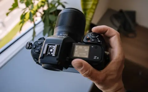 Dłoń trzyma aparat Nikon Z8 z obiektywem 35/1.8 S. Ekran pokazuje ustawienia, a cena tego modelu jest atrakcyjna.