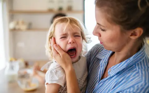 Mama próbuje uspokoić płaczące dziecko, które przeżywa histerię. 5-latek krzyczy, a mama delikatnie trzyma go za policzek.
