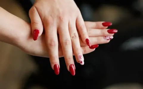 Dłonie z eleganckimi, czerwonymi paznokciami. Niektóre zdobią subtelne, marmurkowe wzory, inne lśnią jednolitą barwą. To prawdziwe tytanowe paznokcie, gotowe na wielkie wyjście.