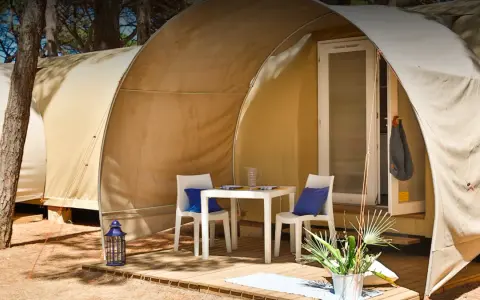 Tavolino e sedie con cuscini blu davanti a una tenda del **Gitavillage Il Gabbiano**. Lanterna blu e piante sul deck.